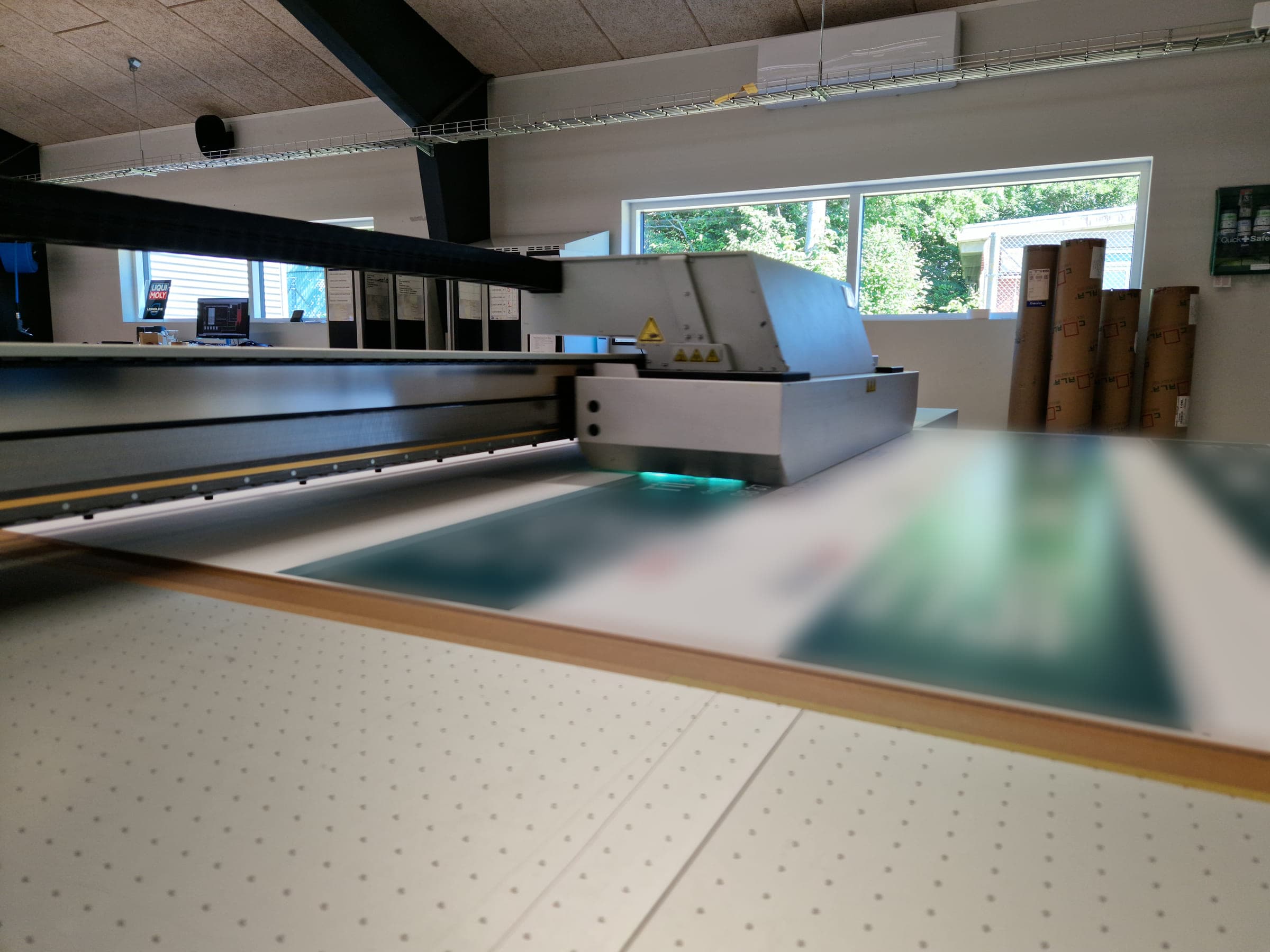 Storformatprinter, der printer på en plade, i et lyst lokale med vinduer.