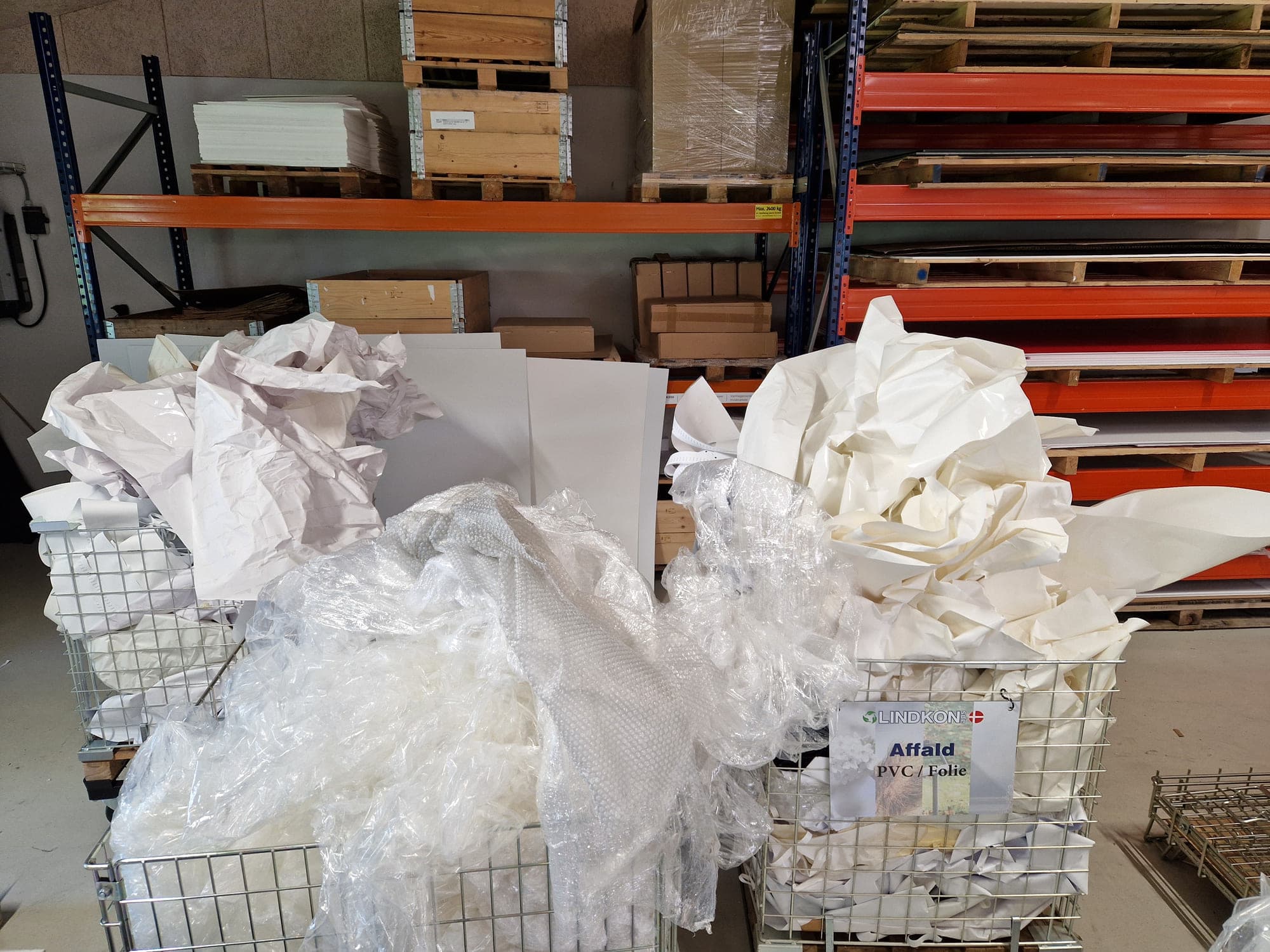 Affald sorteret i trådkurve foran pallereoler; på den ene kurv står ”Affald PVC / Folie”.